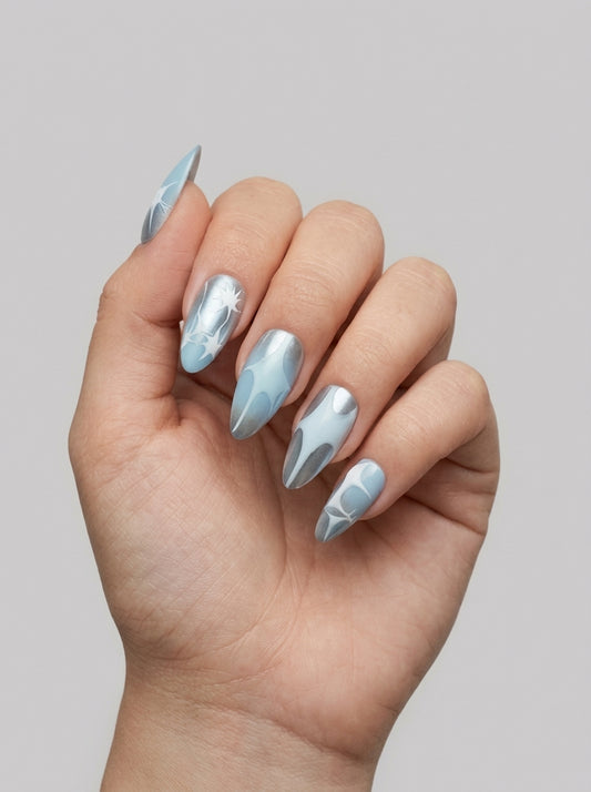 Glacier Chrome – icy blue and silver chrome almond press-on nails with white starburst art worn on hand