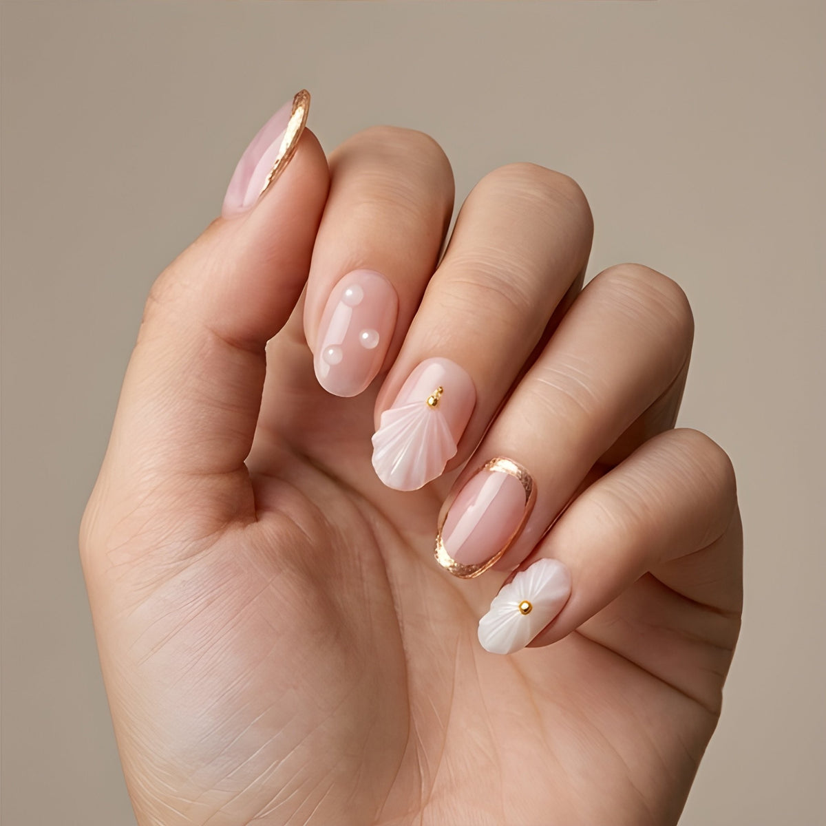 Blush Seashell – blush pink short oval press-on nails with 3D seashells, pearls and gold foil worn on hand