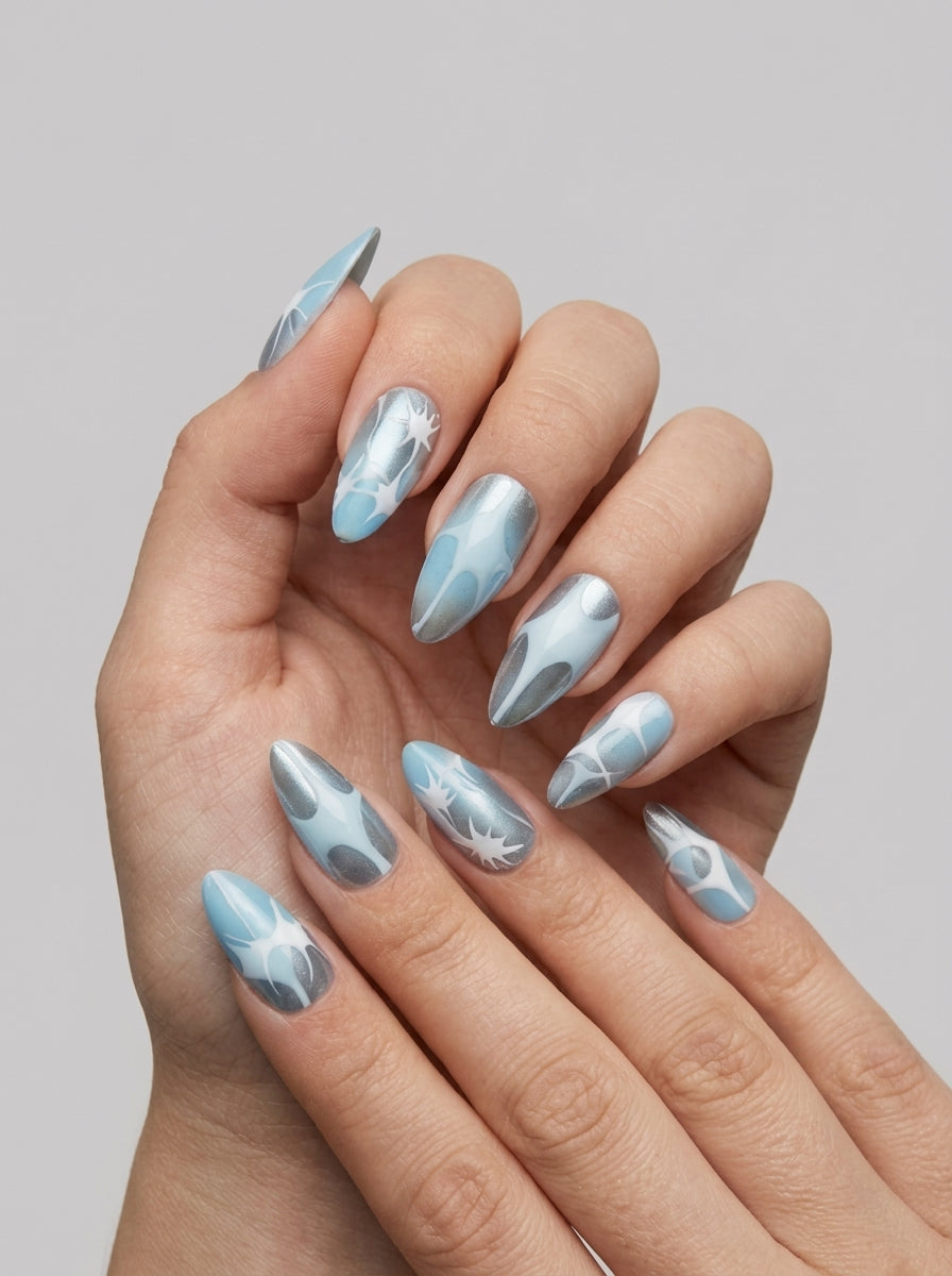Glacier Chrome – icy blue and silver chrome almond press-on nails with white starburst art worn on hand